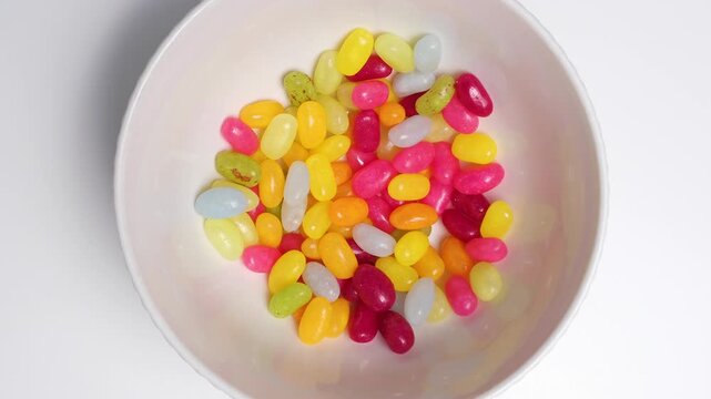 Stop motion of colorful jelly beans constantly changing positions in a white bowl, top view, minimal flat lay, random movement concept. Stop motion food background