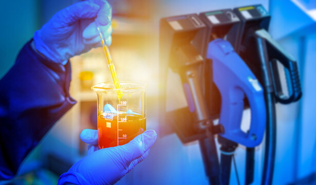Fuel analysis, laboratory testing. Technician mixes liquid sample in beaker near fuel dispenser nozzle, performs chemical quality control and energy product testing.