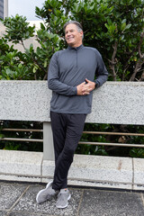 Middle-aged man standing and leaning against speckled planter wall on urban plaza, wearing pullover © wavebreak3