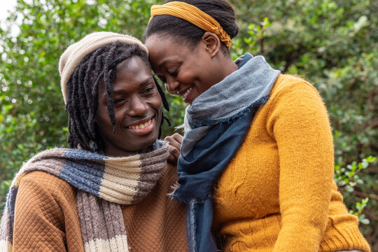 African American couple leaning foreheads together in park, wearing knit scarves and beanie