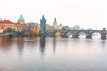 Fototapeta premium Prague Charles Bridge spans the Vltava River, with historic towers and colorful buildings lining the banks. Calm, misty atmosphere reflects the city medieval skyline on the water