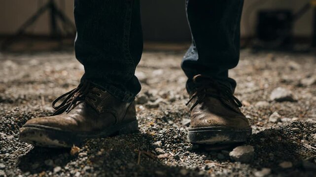 Foley technician manipulating small stones underfoot on a controlled set sharp gravel texture contrasting with the softly obscured studio lights and walls.