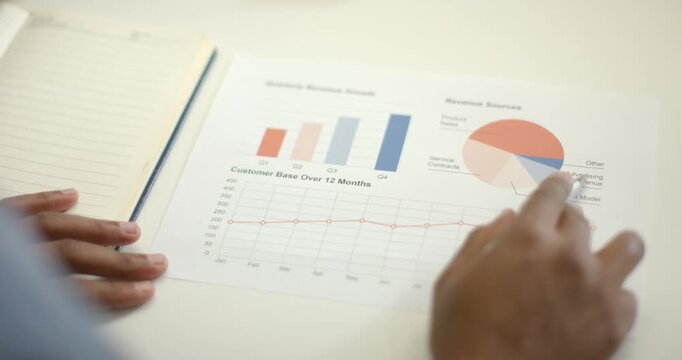 African American man pointing at bars, tapping pie chart on office desk, jotting notes, copy space