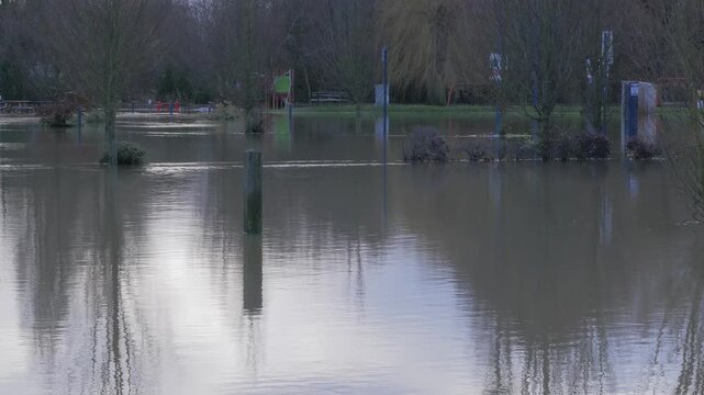 Flooded car park parking lot, signs and meters in flood water, trees in background, wide shot