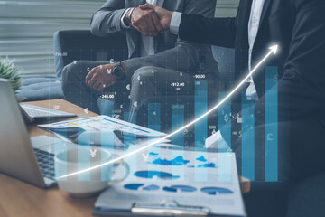 Naklejka premium A close-up view of two professionals shaking hands in a modern office, with financial graphs overlaying the image, symbolizing growth and collaboration. Impute
