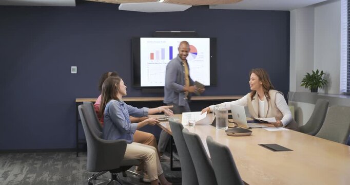 Diverse coworkers in business attire entering conference room, pointing at charts, reviewing data