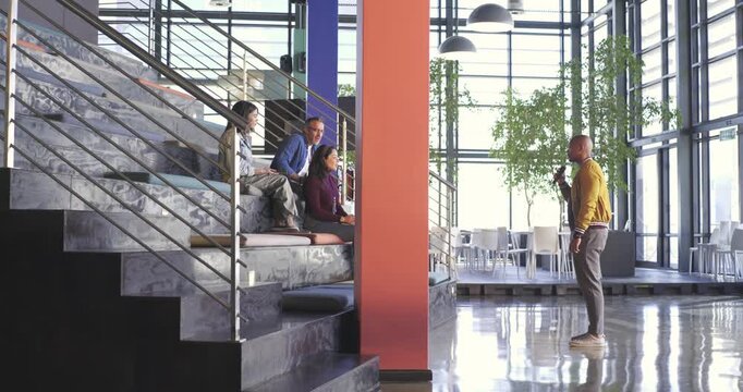 African American man presenting using microphone at atrium pausing after colleague raising hand