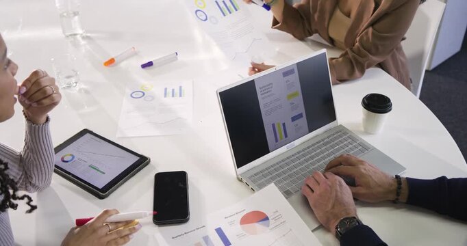 Leaning in, three colleagues are examining charts around table and jotting notes to plan actions