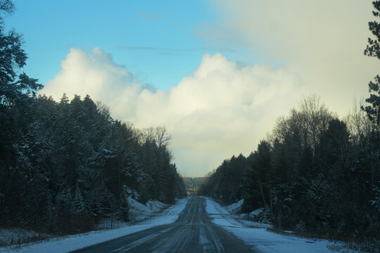 Big clouds loom over an icy highway through the forest.