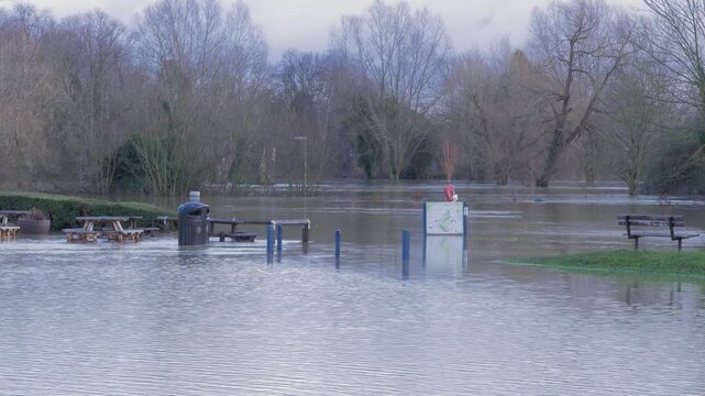 Flooded car park, picnic area, riverside park, wooded town rural park covered in flood water, picnic tables, waste bin, signpost submerged