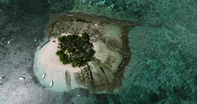 Rocky coastline with small tropical island covered in coconut trees surrounded by blue sea water. Siargao, Philippines.