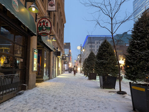 Canada, Montreal, 23 December 2025 : Snowy evening on bustling city street with festive decorations.