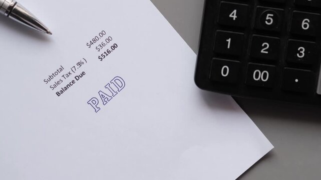 Close up of paid stamp being pressed onto invoice with calculator and pen nearby