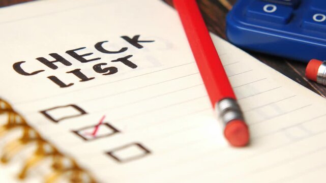 Close up of checklist on notepad with red checkmark and pencils, business planning concept