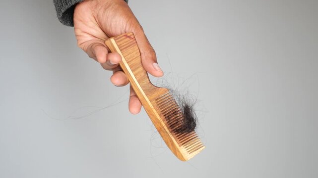 Close up of hand holding a wooden comb with a large amount of tangled black hair, indicating hair loss and need for hair care