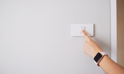Close-up of a hand turning off light switch on wall. Energy saving, cost saving and home electricity concept