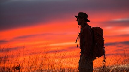 Silhouette of a Hiker Standing in a Field Against a Vibrant Sunset Sky with Dramatic Colors on the Horizon
