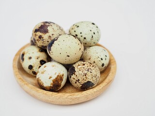 Fototapeta premium Quail eggs are placed on a wooden plate on a white background.