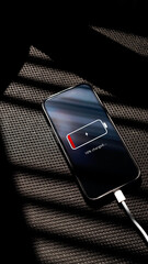Smartphone with low battery 10% charging via cable on a black chair textured surface. Concept representing power shortage, energy management