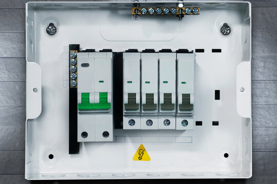 Close-up front view of a modern electrical distribution board with miniature circuit breakers (MCB) and grounding busbar installed inside a white metal enclosure. The panel features green and gray swi