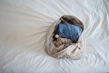 Bag with clothes and items on bed in a room