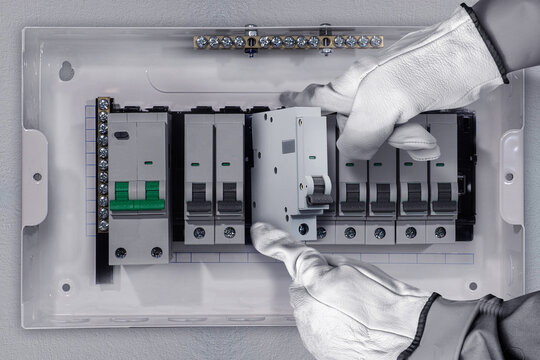 Close-up of a professional electrician wearing protective gloves installing a miniature circuit breaker (MCB) inside an electrical distribution board. Concept of electrical maintenance, safety standar