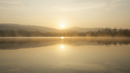 Obraz premium Serene sunrise over misty lake with golden light and distant hills