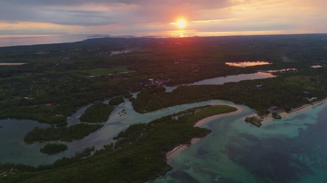 Wide aerial drone view of the sun setting over the lush mangrove landscape and coastal waters of Bantayan Island