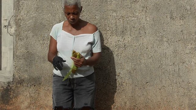 A Woman Husking a Caterpillar Damaged Corn