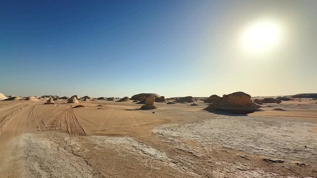 Fast motion through desert rock formations surrounded yellow sand with car tracks under bright sun and blue sky