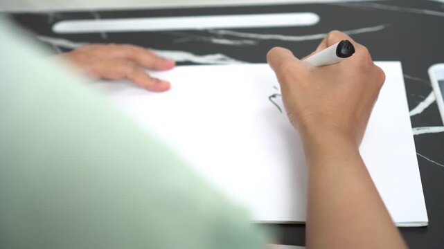 a woman is writing the Arabic sentence Basmalah or Bismillahirrahmanirrahim which has the meaning of saying the name of Allah, the Most Gracious and Most Merciful, using a black marker on white paper