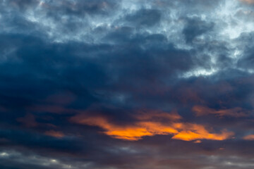 Obraz premium Dramatic view of a darkening sky where bright orange light breaks through thick layers of blue and grey clouds