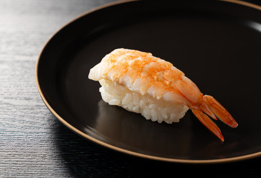 Close-up of premium ebi (shrimp) nigiri sushi on a black plate against a dark background