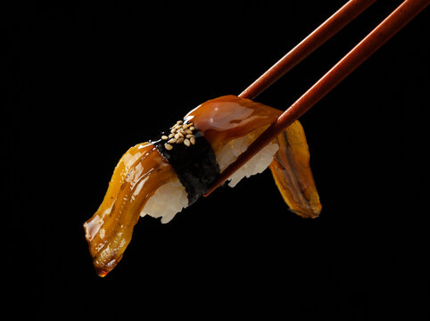 Close up of chopsticks holding eel nigiri sushi with sweet sauce on black background