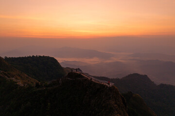 Aerial view of a mountain ridge path with a fence overlooking a breathtaking valley and sea of clouds at sunrise.