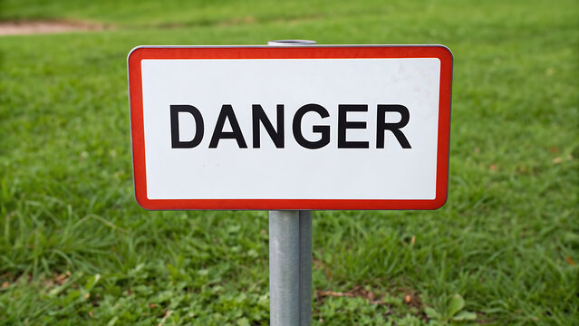 A red and white danger sign standing in a grassy field with a clear blue sky.