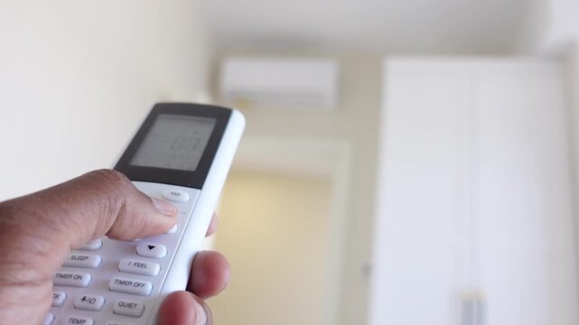 Person using air conditioner remote control to adjust home temperature and cooling settings indoors