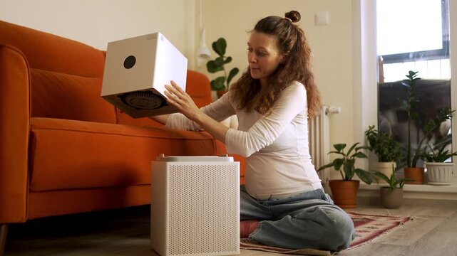 Surprised young woman unwrapping an air purifier and finding a filthy filter coated in dust and grime, coming to understand the necessity of regular care for ensuring healthy indoor air