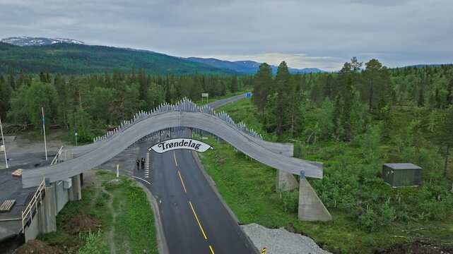 Aerial drone view of Tr&oslash;ndelag boundary bridge over a road in Norway. Norwegian Tr&oslash;ndelag sign spans the arch above passing traffic and pine forest.