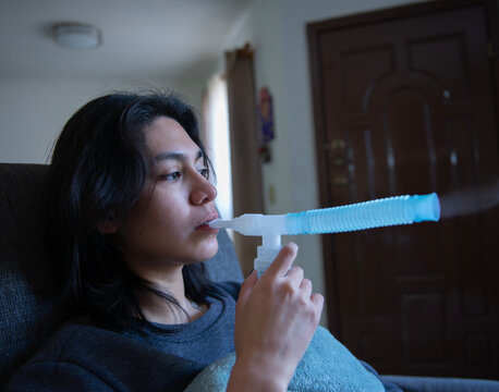 Mujer joven hispana Mexicana en tratamiento de nebulizacion en casa por problemas respiratorios de bronquitis y asma.