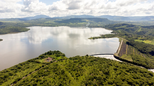 Aerial view of a lake with dam surrounded by green mountains.