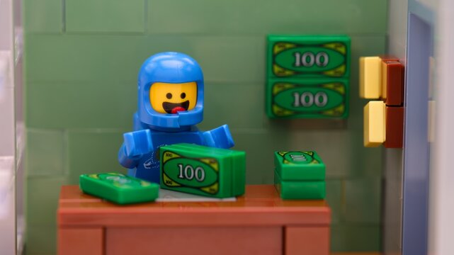 Tambov, Russian Federation - May 26, 2025 Lego Benny astronaut minifigure sitting in his office with money.
