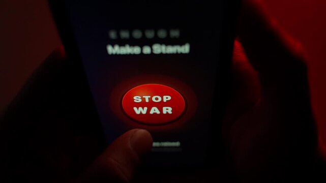 A finger presses the STOP WAR button on the smartphone screen and puts it out of focus. The big red button in the center of the screen