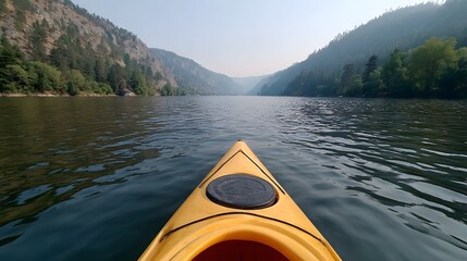 Obraz premium A yellow kayak glides down a wide river flanked by tree covered mountains under a hazy sky