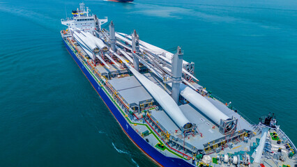 Large heavy lift cargo ship transporting massive wind turbine blades across the deep blue ocean. Global logistics for renewable energy and maritime shipping industry business concept. © Yellow Boat