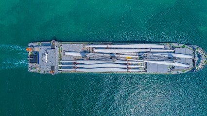 Large heavy lift cargo ship transporting massive wind turbine blades across the deep blue ocean. Global logistics for renewable energy and maritime shipping industry business concept.