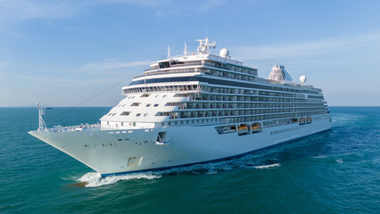 Majestic white luxury cruise ship sailing across the deep blue ocean water on a bright sunny day. Summer vacation, tropical travel destination, and global tourism industry concept.