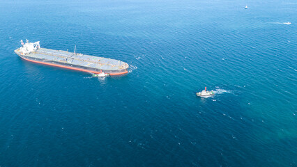 Fototapeta premium Massive crude oil tanker ship assisted by tugboats while sailing across the deep blue ocean. Global maritime logistics, fossil fuel energy, and heavy industrial transport business concept.