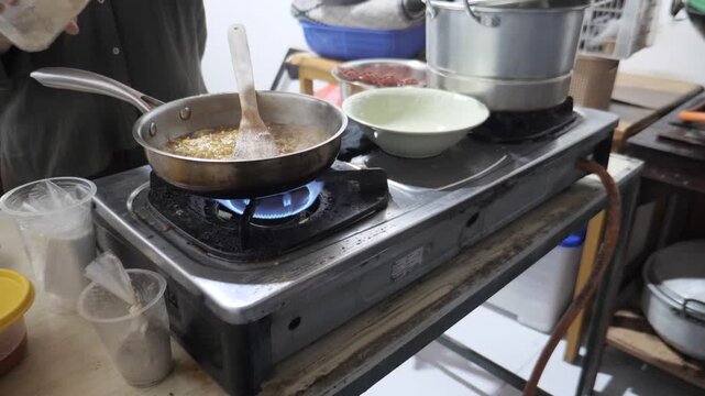 Anonymous woman cooking instant noodles or "Mie Nyemek" in a pan, stirring noodles with savory thick sauce and spices in a home kitchen