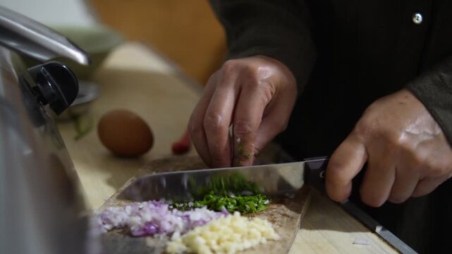 Close up of anonymous woman hands chopping and slicing fresh green celery or coriander leaves on a wooden cutting board